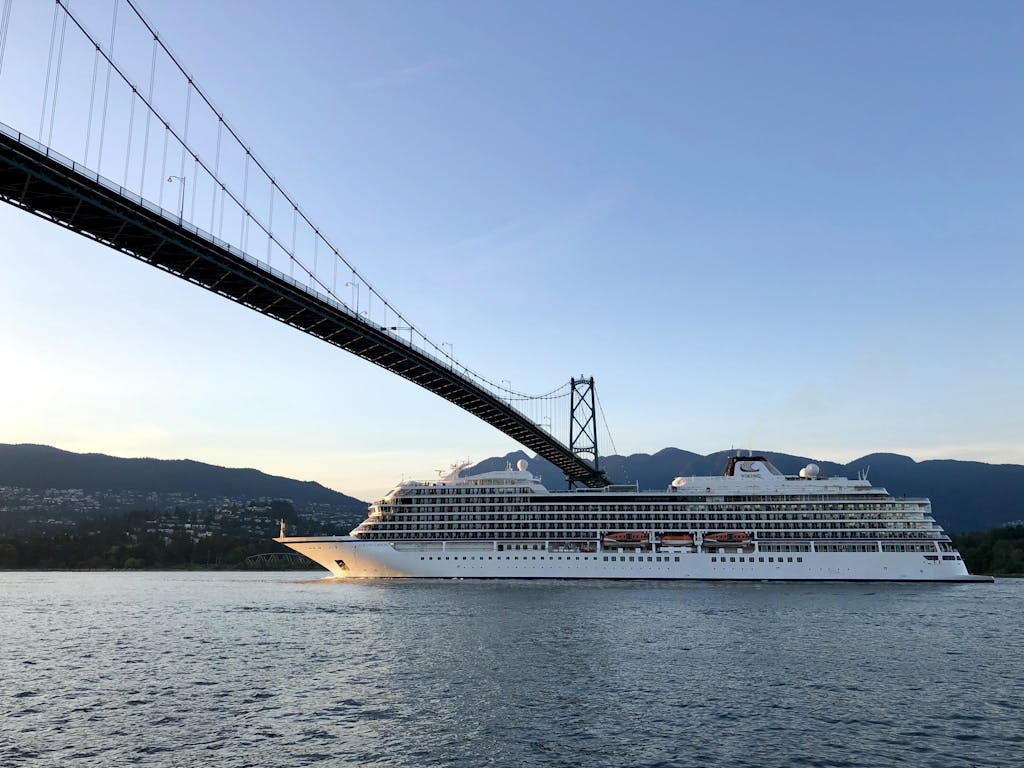 A cruise ship sails under the iconic Lions Gate Bridge in Vancouver, BC, at twilight.