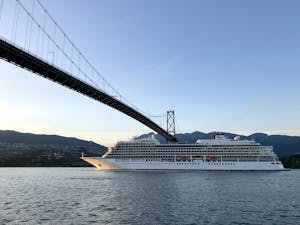 A cruise ship sails under the iconic Lions Gate Bridge in Vancouver, BC, at twilight.