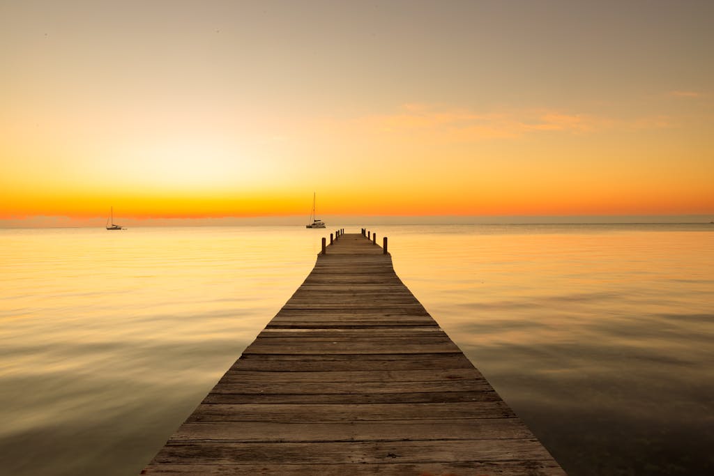 Wooden pier extends into tranquil sea at sunset in Belize, creating a warm, peaceful scene.