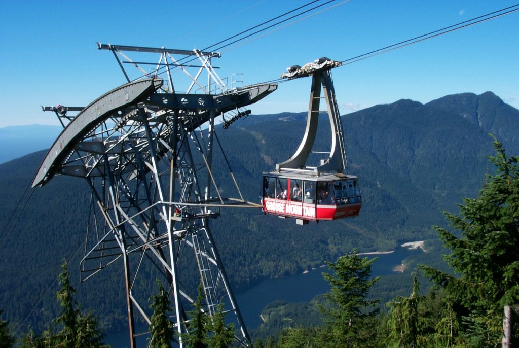 The godola headed up Grouse mountain. The red car is suspended in the air with Capilino Lake in the background